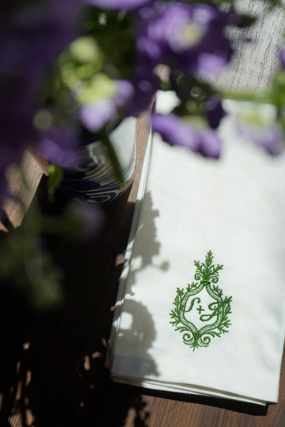 White napkin with green emblem on a wooden surface with purple flowers in the background